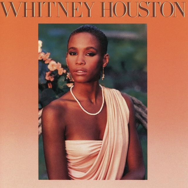 Whitiney Houston em um vestido bege com colar de pérolas sentada em um jardim, para a capa do seu primeiro álbum.