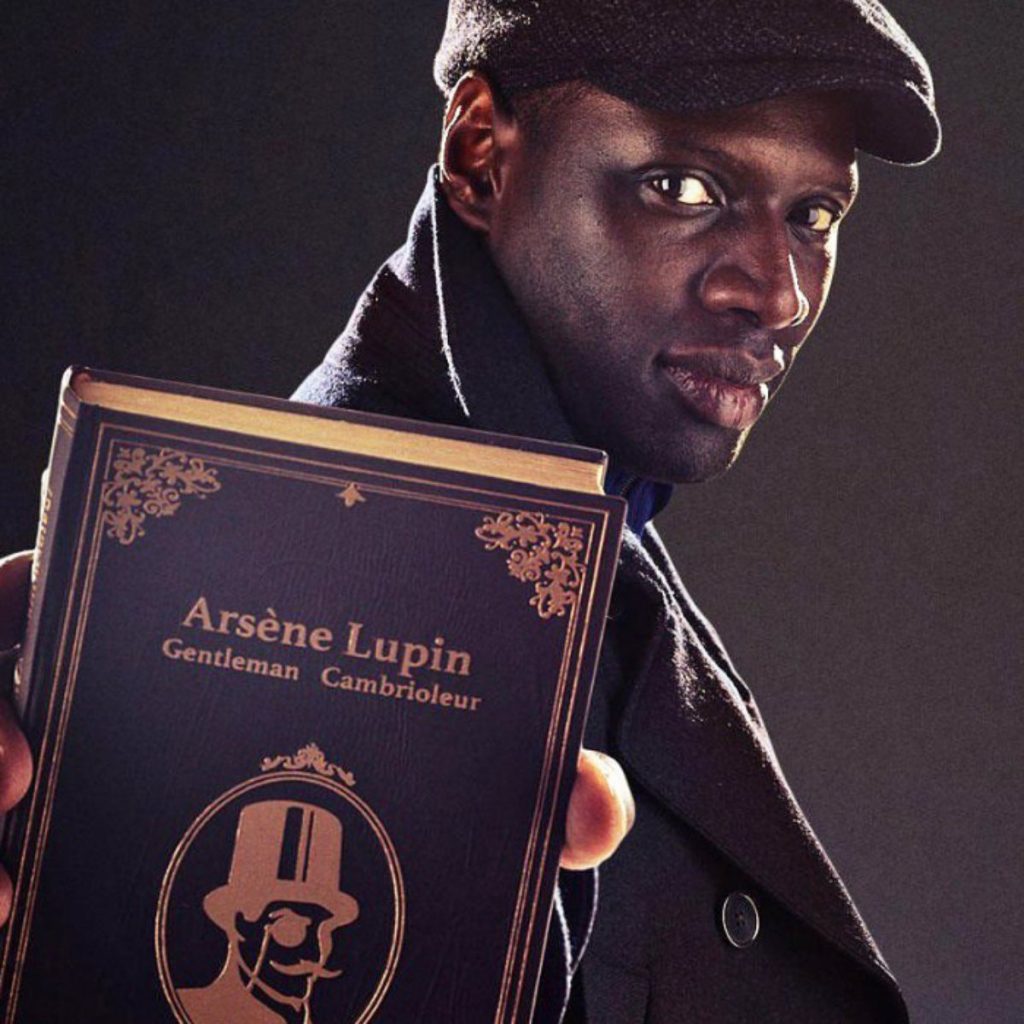 Omar Sy segura um livro de Arsène Lupin em um fundo preto.